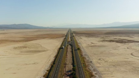 Flying over an expansive highway with a steady stream of trucks and vehicles crossing the arid landscape.