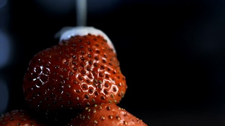 Fresh cream being poured onto strawberries.