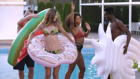 Friends dancing with floats beside a swimming pool