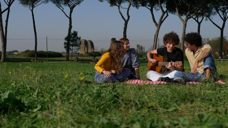 Friends in a park singing along to guitar.