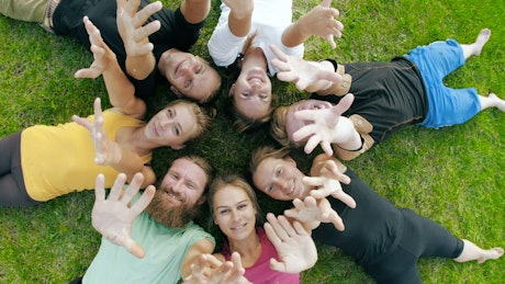 Friends lying on the grass waving at the camera