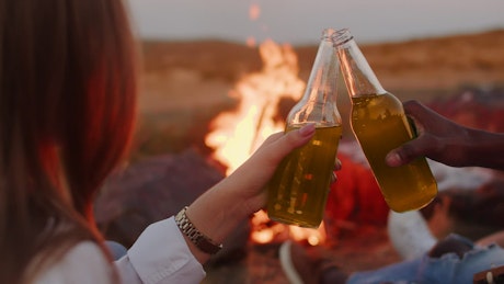 Friends sharing a beer next to a campfire.