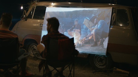 Friends watching a movie projected on the van