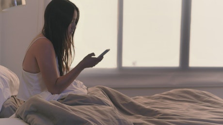 Girl checking her cell phone in her bed upon waking.