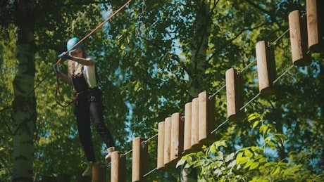 Girl crossing with a harness over a rope bridge.