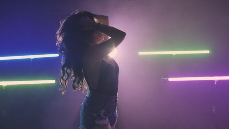 Girl dancing on a dark floor under colored lights.