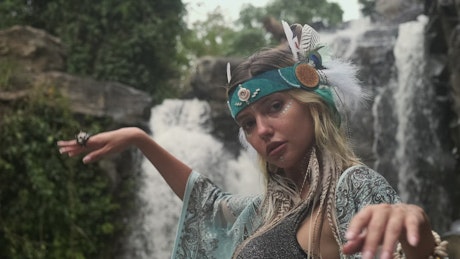 Girl dressed in tribal style and posing next to waterfall.