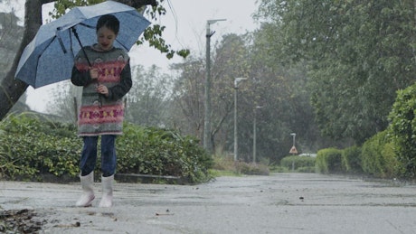 Girl jumping in puddles of water in the rain.