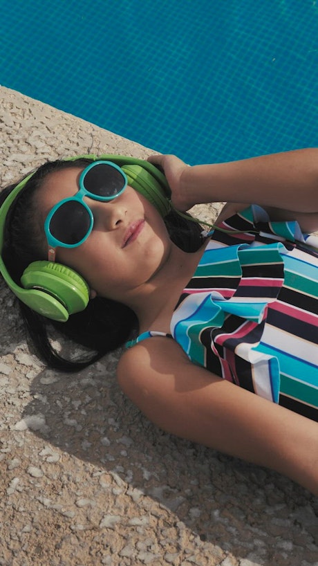 Girl listening to music next to a pool.