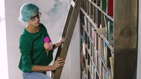 Girl on a ladder looking in a huge bookcase.