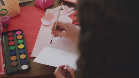 Girl painting hearts on a valentine card.