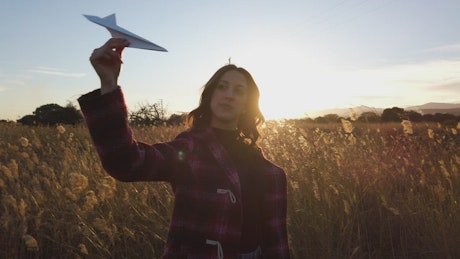 日落时分，女孩在田野里玩纸飞机