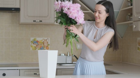 Girl prepares bouquet of flowers and puts it in a white vase.