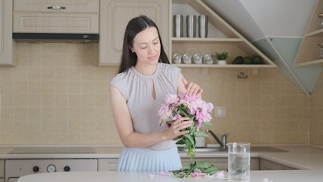 Girl prepares bouquet of pink flowers and puts it in glass vase.