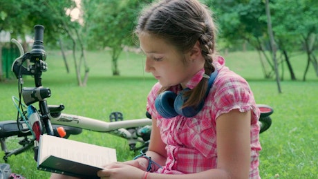 Girl reading outside next to her bike