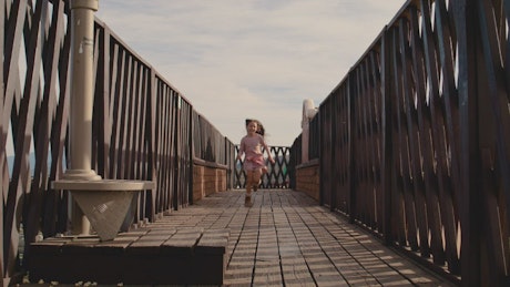 Girl running happily across a wooden bridge.