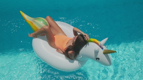 Girl sitting on unicorn ring in swimming pool.