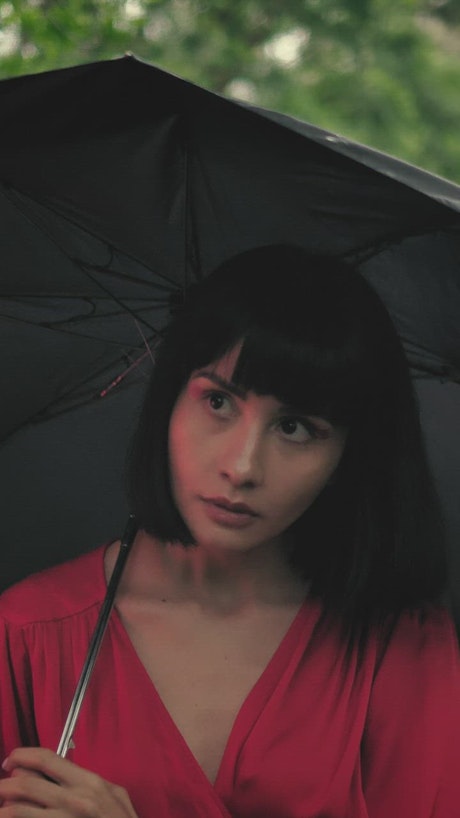 Girl walking through a park with an umbrella in the rain.