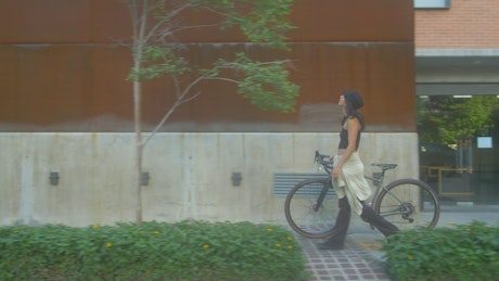 Girl walking with a bicycle on the sidewalk.