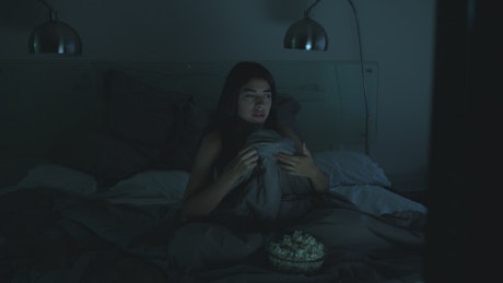 Girl watching a horror movie in her bedroom with the lights off