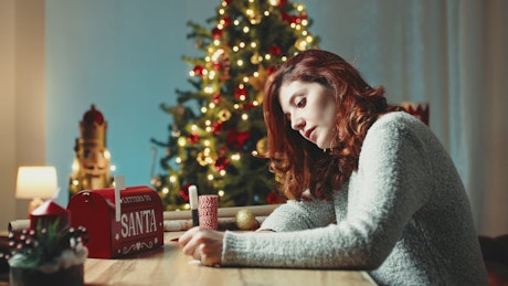 Girl writing letter to Santa with Christmas tree in the background.