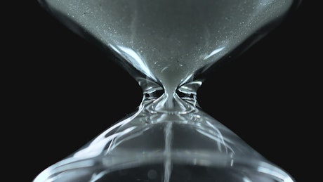Glass hourglass close up on a black background.