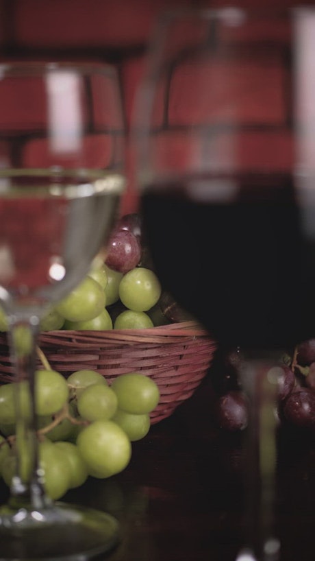 Glasses with red and white wine with a basket of grapes behind.