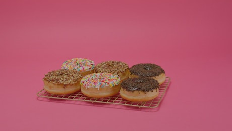 Glazed donuts of different flavors on a pink background.
