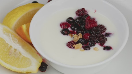 Granola being dropped on a plate with yogurt and berries.
