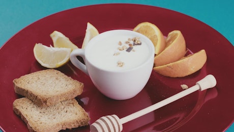 Granola drops to a bowl with yogurt on a plate with fruit and toast.