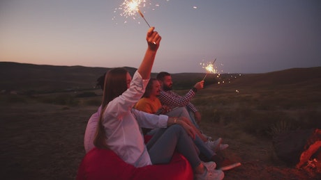 Group of happy friends hold sparklers out in nature.