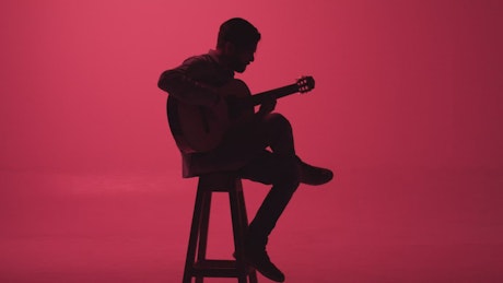 Guitarist playing in the dark on a pink background.