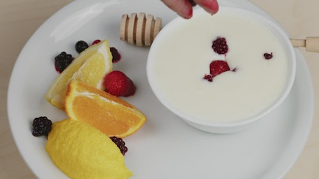 Hand drops berries on a plate with yogurt.