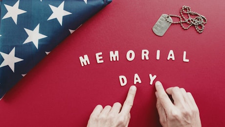 Hand forms the word Day on red background commemorating Memorial Day.