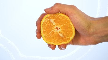Hand of a person squeezing an orange on a light background.