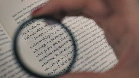 Hand of a person using a magnifying glass to read a book.