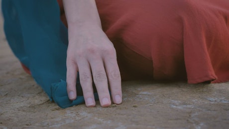 Hand of a woman touching the ground with wind moving her clothes.