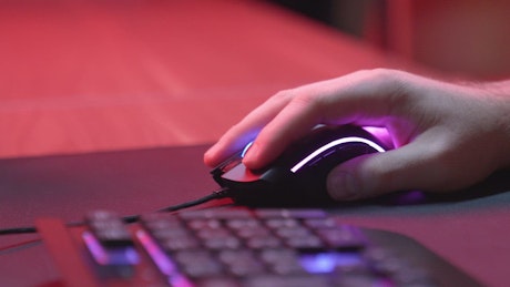 Hand using a gaming mouse with RGB lighting.