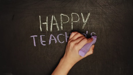 Hand writes 'Happy Teacher's Day' message on chalkboard.