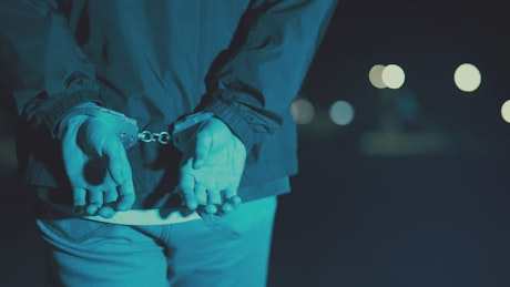 Handcuffed man walking to a police car.