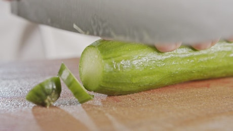 Hands of a cook cutting a cucumber.