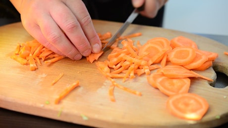 Hands of a person chopping carrots on a board.