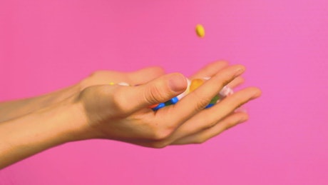Hands of a person full of sweets on a pink background.