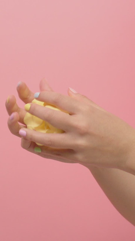 Hands of a woman playing with yellow plasticine.