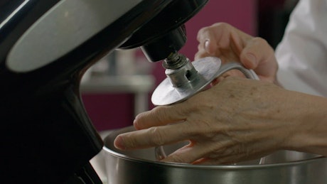 Hands of an elderly confectioner preparing a mixer.
