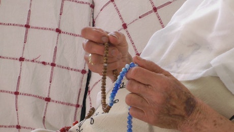 Hands of old woman praying with the rosary.
