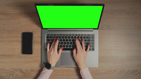 Hands typing on a keyboard with a green screen laptop.