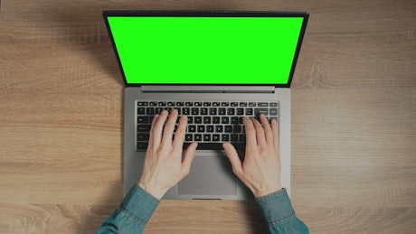 Hands typing with a green screen laptop.