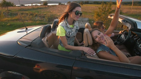 Happy girls traveling in a convertible car at sunset.