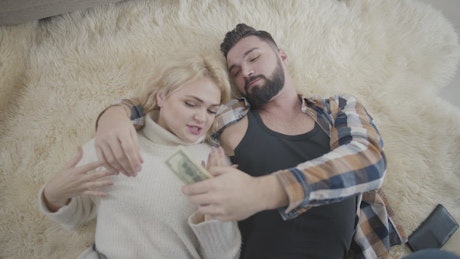 Happy rich couple lay on rug and count cash